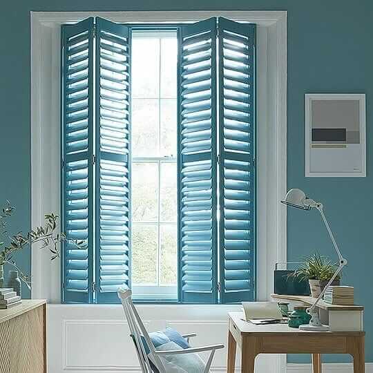 A room with blue shutters and a desk.