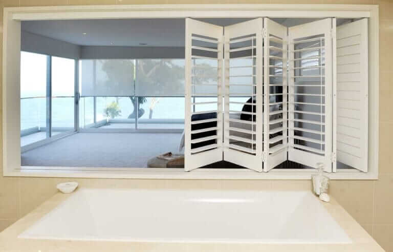 A bathroom with white shutters and a bathtub.